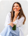 Woman smiling while holding a green smoothie in a jar.