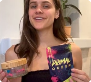 Woman holding a Primal Queen product package and a glass container, smiling at the camera.