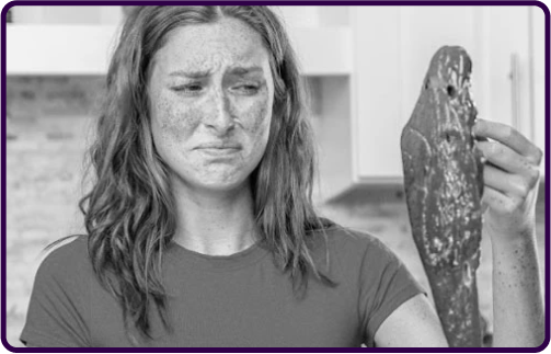 A woman looking disgusted while holding a raw piece of meat in a kitchen.