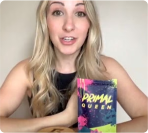 Woman holding a colorful product package labeled 'Primal Queen.'