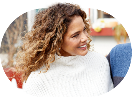 A woman with curly hair smiles while looking to the side.