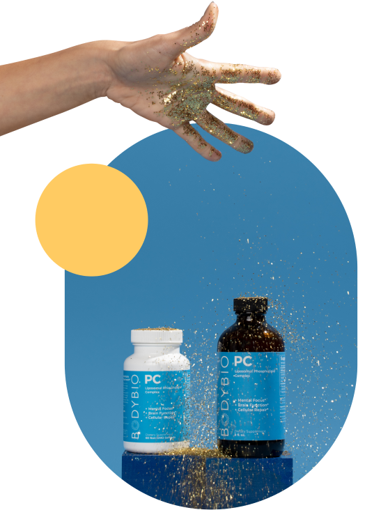 Hand sprinkling glitter over two BodyBio supplement bottles on a blue background.