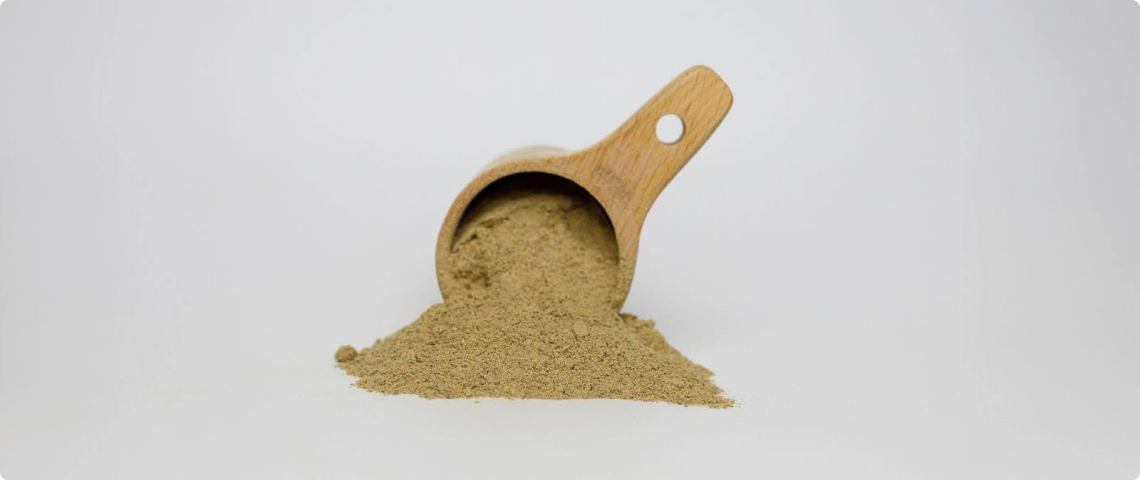 Wooden scoop with spilled brown powder on a white background.