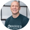Smiling person wearing an 'Obsessed Garage' t-shirt.