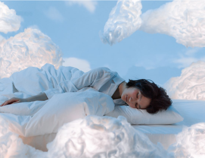 A person sleeping peacefully on a bed surrounded by fluffy clouds in the sky.