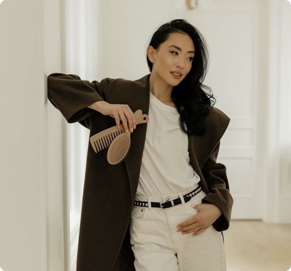 Person in a brown coat holding a hairbrush in a bright room.