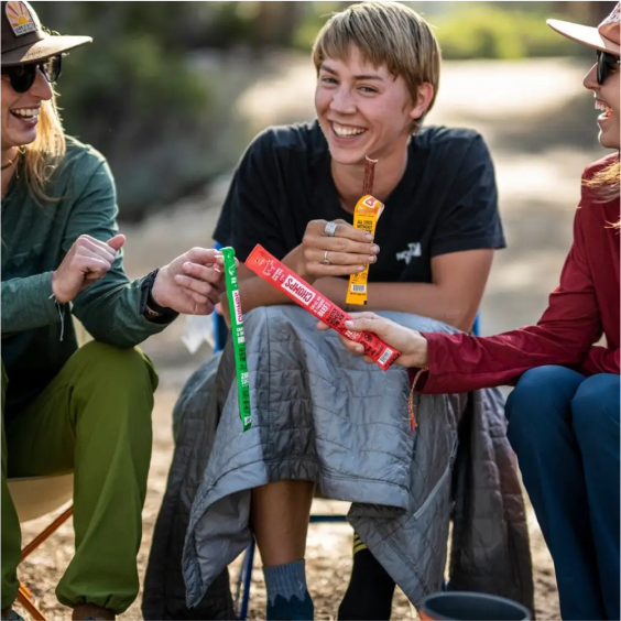 Three people laughing and enjoying snacks while sitting outdoors.