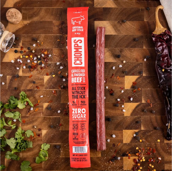 Packaged beef stick on a cutting board with spices and herbs.