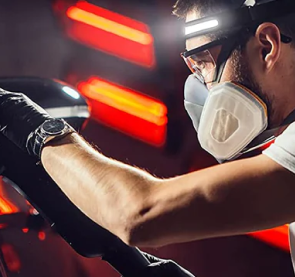 Person polishing a car while wearing safety gear and mask.