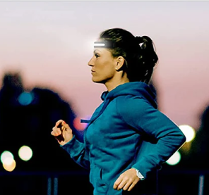 Woman jogging at dusk with a headlamp, wearing a blue hoodie.