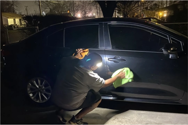 Person polishing a black car at night using a headlamp for light.