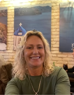 A woman smiling indoors with scenic wall art in the background.