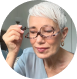 Older person adjusting glasses, wearing a light blue shirt, indoor setting.