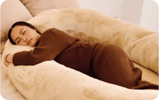 Person sleeping comfortably on a large, cozy, beige cushion.