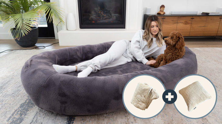Woman and dog relaxing on large, plush bed near a fireplace.