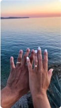 Two hands with rings displayed against a sunset over the ocean.