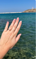 Hand with engagement ring over clear blue water background.