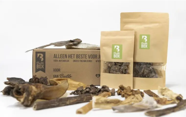 Various dried natural dog treats in front of labeled packaging.