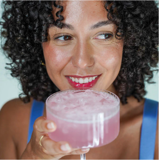 Smiling woman enjoying a pink drink in a glass.