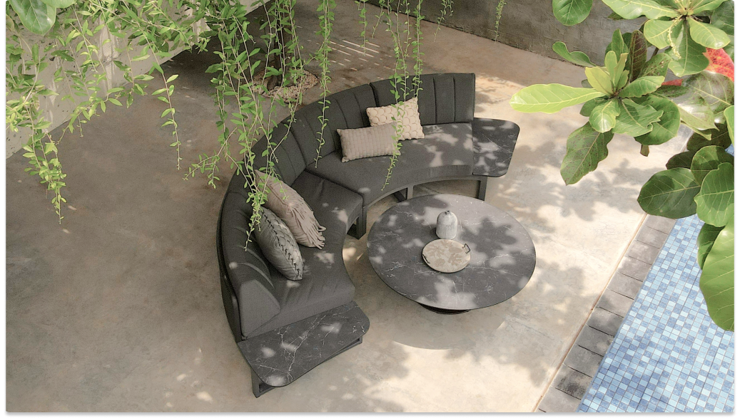 Outdoor seating area with a curved sofa, round table, and lush greenery.