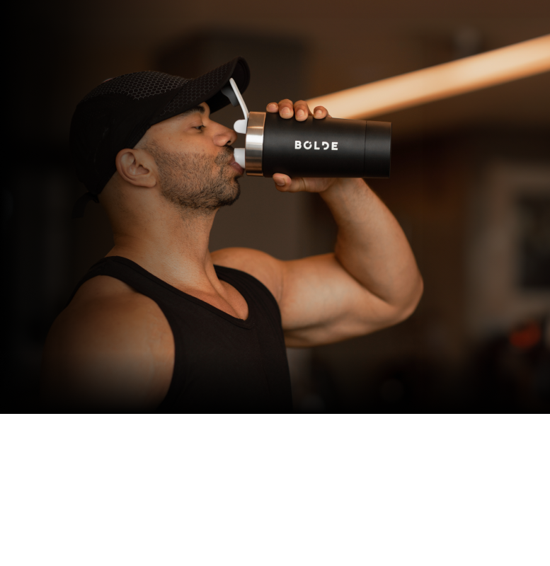 Man drinking from a black water bottle in a gym setting.