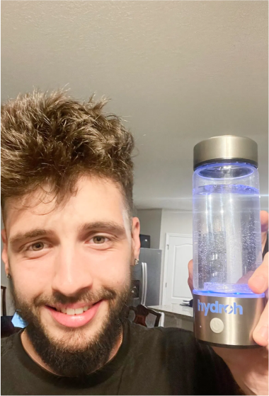 A person smiling while holding a glowing water bottle with a metal base.