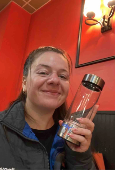 Person smiling and holding a clear bottle in a warmly lit room.