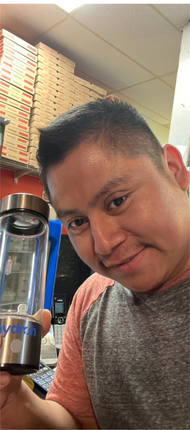 Person smiling while holding a clear water bottle in a room with stacked boxes.