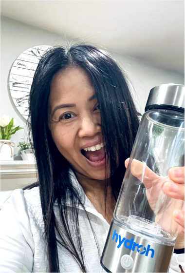 Person smiling and holding a Hydroh water bottle indoors.