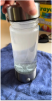 A hand holding a glass water bottle with fogged interior, placed on a blue cloth.