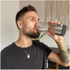 Man drinking water from a clear glass with a neutral background.