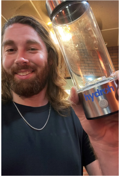 Man holding a clear reusable water bottle with 'hydrzh' branding.