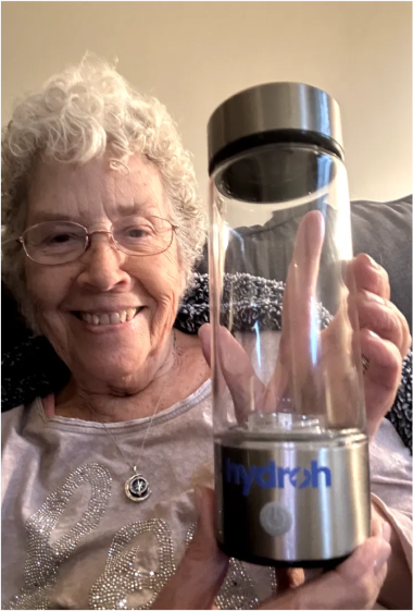 Smiling woman holding an empty HydroH bottle while sitting on a couch.