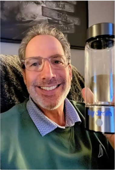 Man smiling and holding a clear MyHydralife bottle indoors.