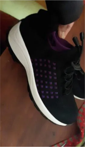A hand holding a black sneaker with white soles and purple accents.