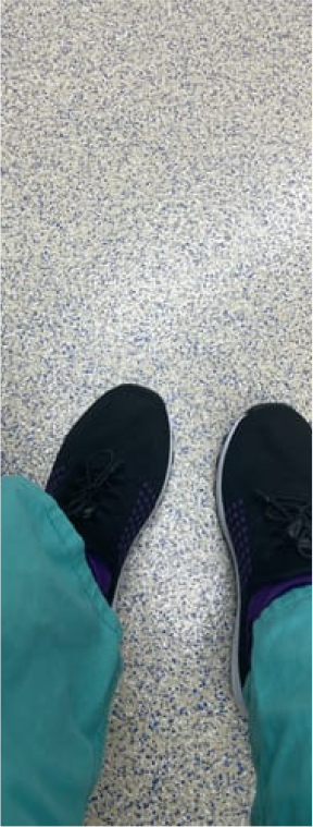 Person wearing black shoes and teal pants on a speckled floor.