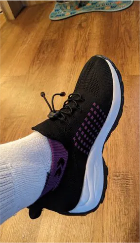 A person wearing black and purple sneakers with white socks on a wooden floor.