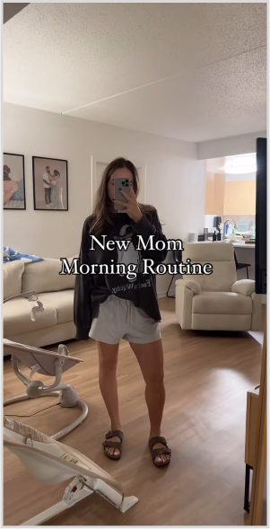 Woman taking mirror selfie in living room, with 'New Mom Morning Routine' text overlay.