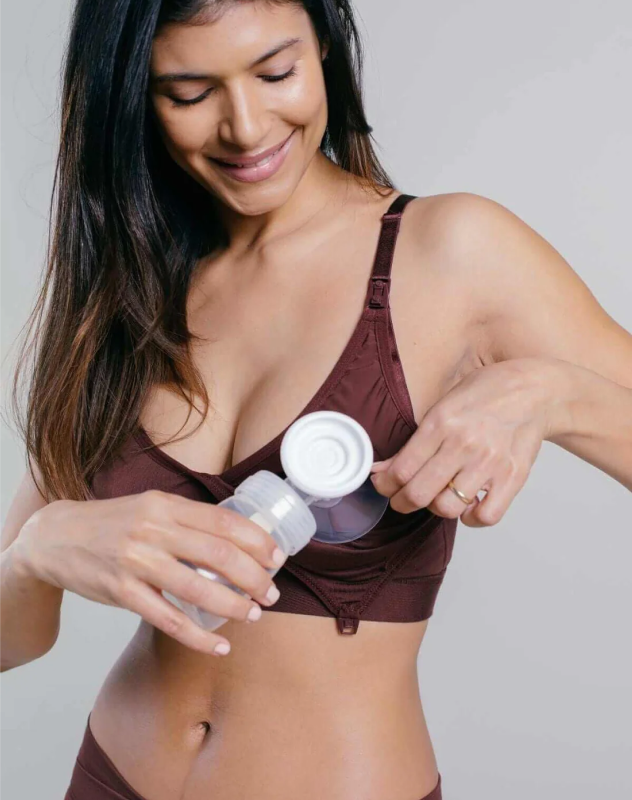 Woman using a breast pump, smiling while adjusting pump bottle.
