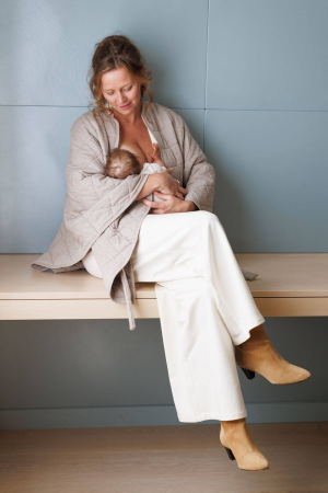 A woman sitting on a bench, holding a baby tenderly.
