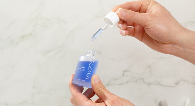 Hand holding a blue serum bottle with a dropper on a marble background.