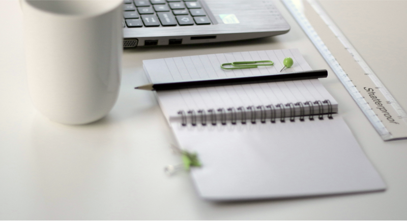 Office desk with a notebook, pen, laptop, coffee mug, and a ruler.