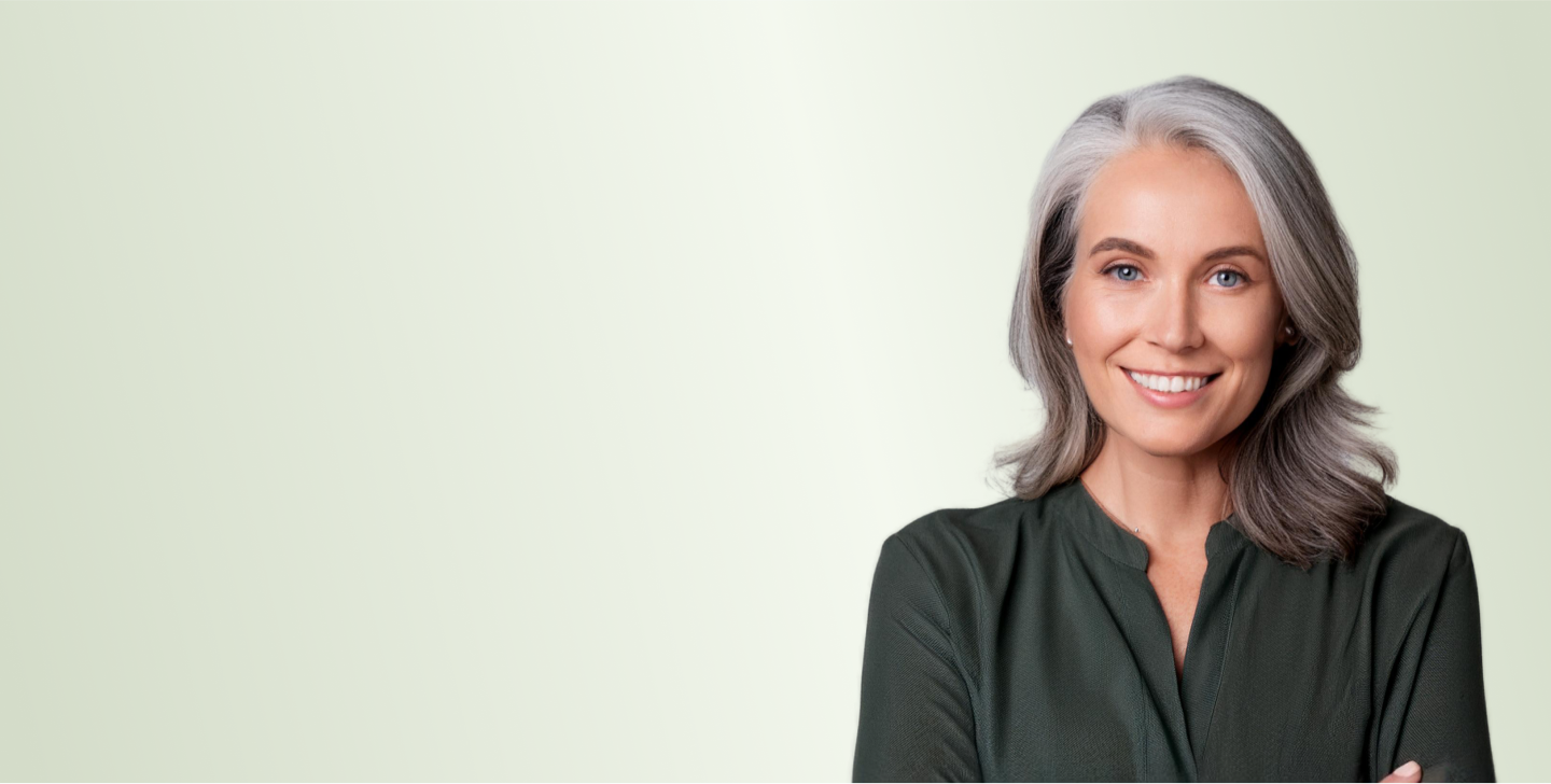 Smiling woman with gray hair and green blouse on a light green background.