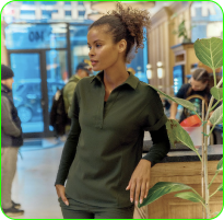 A person in a green shirt leans on a counter indoors, with plants nearby.