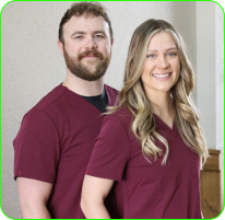 Two people in matching burgundy scrubs smiling, standing indoors.