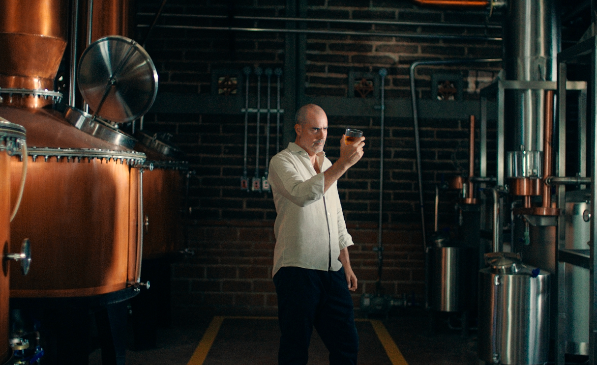 Man inspecting a glass of liquid in a distillery.