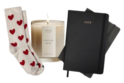 Cozy scene with heart-patterned socks, a 'Vintage Rose' candle, and a personalized black notebook.