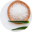A wooden bowl filled with coarse salt, accompanied by green leaves.