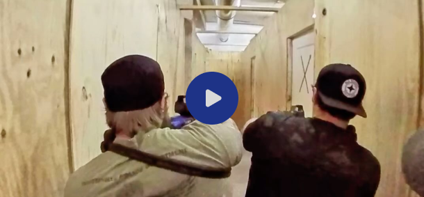 Two individuals aiming firearms down a wooden hallway.