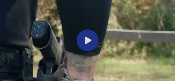 Close-up of a holstered gun and a tattooed ankle outdoors.